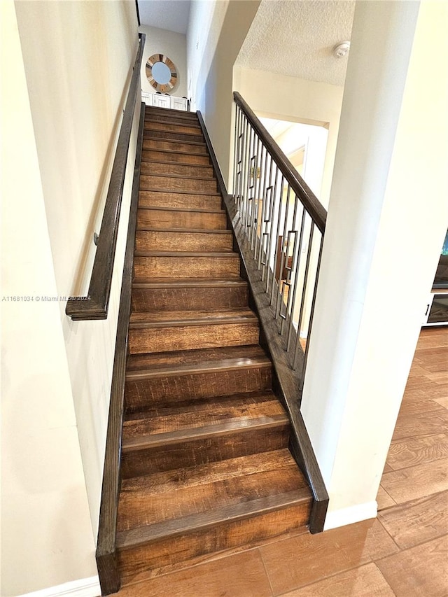 stairs with a textured ceiling and wood-type flooring