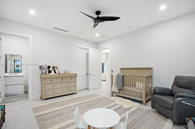 bedroom with a crib, connected bathroom, and ceiling fan