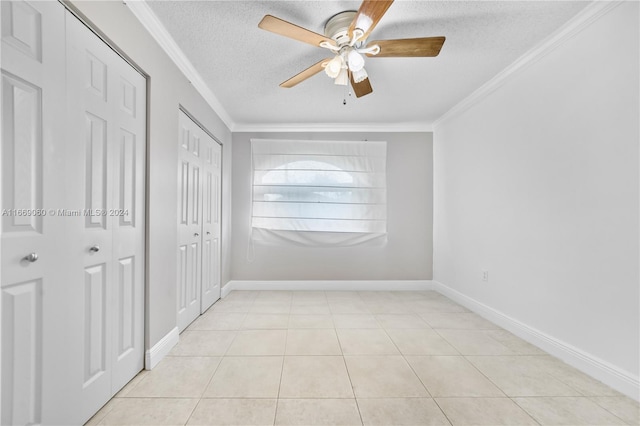 empty room with ceiling fan, a textured ceiling, light tile patterned floors, and crown molding