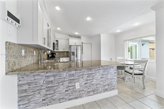 kitchen featuring light stone counters, white cabinets, kitchen peninsula, stainless steel refrigerator with ice dispenser, and sink