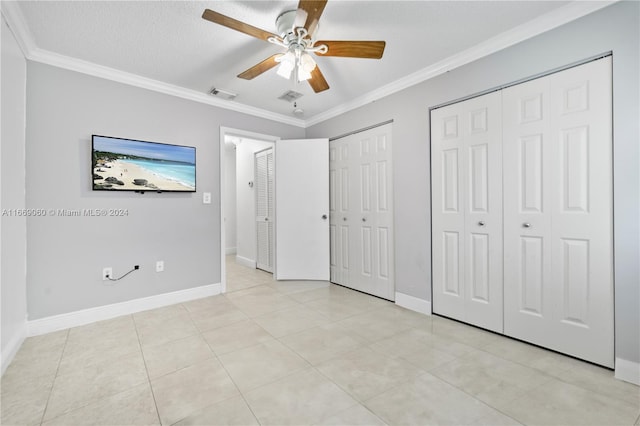 unfurnished bedroom with a textured ceiling, light tile patterned floors, ceiling fan, crown molding, and multiple closets