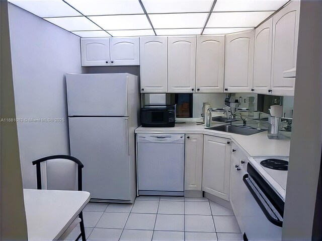 kitchen with sink, white appliances, light tile patterned floors, white cabinetry, and a drop ceiling