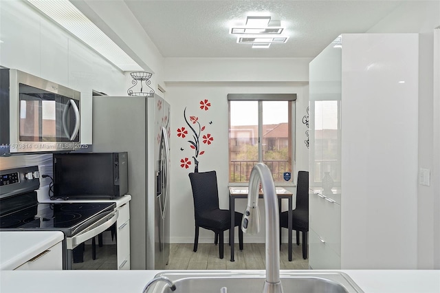 kitchen featuring white cabinetry, sink, a textured ceiling, appliances with stainless steel finishes, and light wood-type flooring