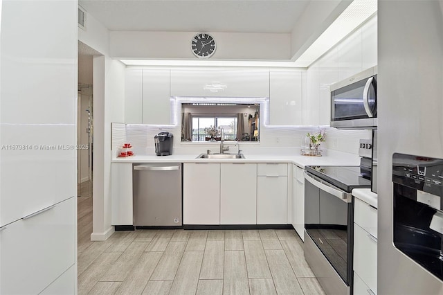 kitchen featuring stainless steel appliances, a sink, white cabinetry, light countertops, and modern cabinets