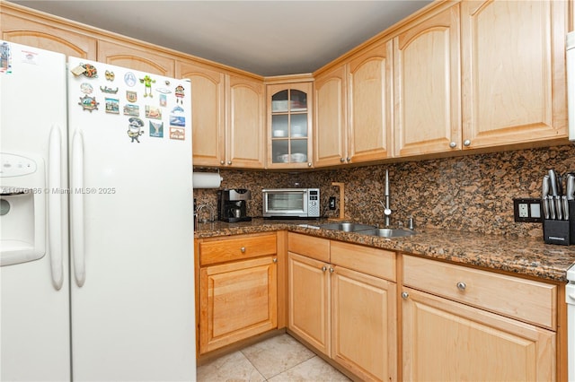 kitchen with dark stone counters, sink, decorative backsplash, white fridge with ice dispenser, and light tile patterned flooring