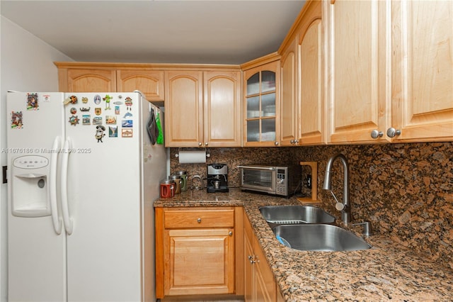 kitchen with white fridge with ice dispenser, sink, backsplash, dark stone counters, and light brown cabinetry