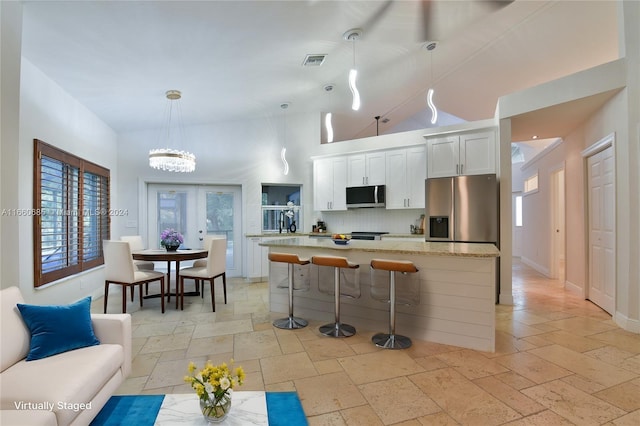 kitchen with light stone countertops, white cabinetry, stainless steel appliances, pendant lighting, and a center island with sink