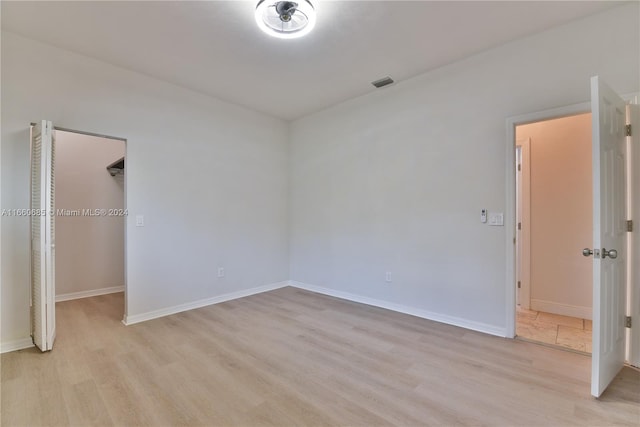 unfurnished bedroom with a spacious closet, a closet, and light wood-type flooring