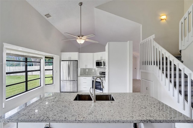 kitchen featuring light stone countertops, high vaulted ceiling, appliances with stainless steel finishes, and sink