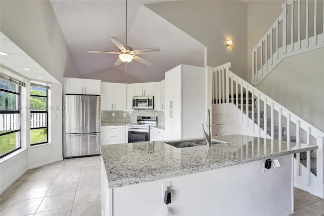 kitchen featuring stainless steel appliances, sink, white cabinetry, light stone counters, and high vaulted ceiling