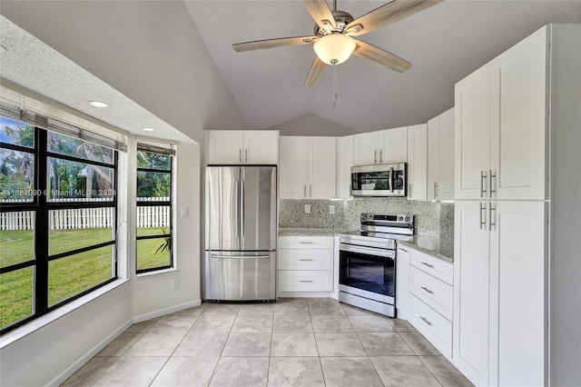 kitchen with lofted ceiling, a wealth of natural light, white cabinetry, appliances with stainless steel finishes, and light stone counters