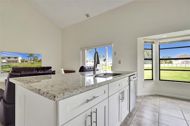 kitchen featuring sink, white cabinetry, vaulted ceiling, light stone counters, and a center island with sink