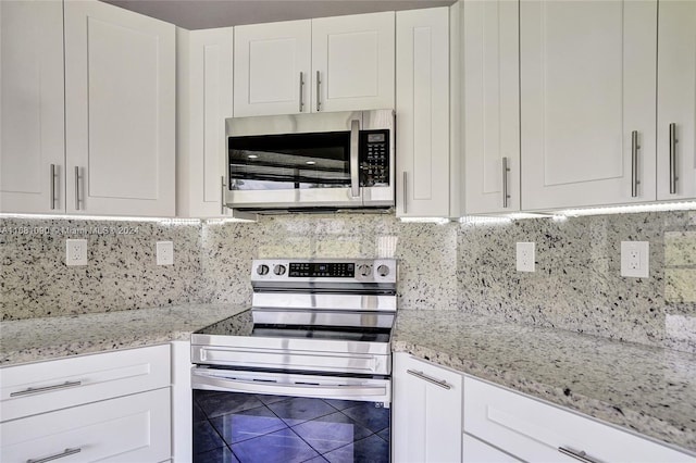 kitchen with white cabinetry, light stone countertops, stainless steel appliances, and backsplash