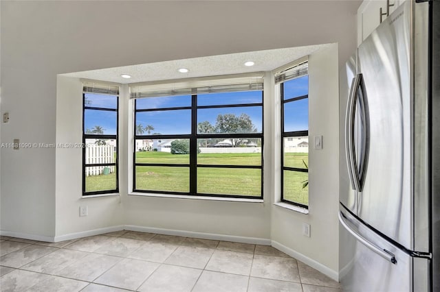 kitchen with a healthy amount of sunlight, stainless steel refrigerator, light tile patterned floors, and white cabinets