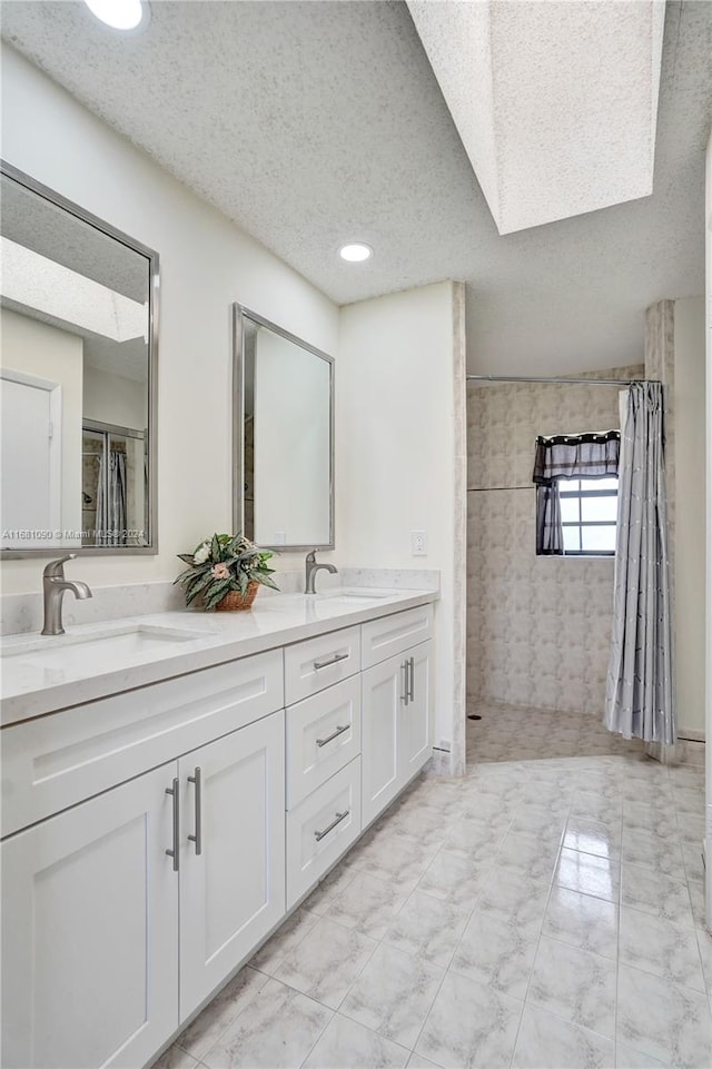 bathroom with vanity, a skylight, a textured ceiling, and walk in shower