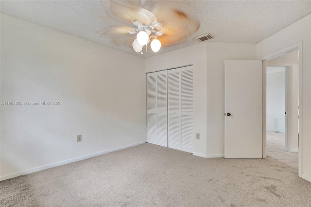 unfurnished bedroom featuring light carpet, a textured ceiling, a closet, and ceiling fan