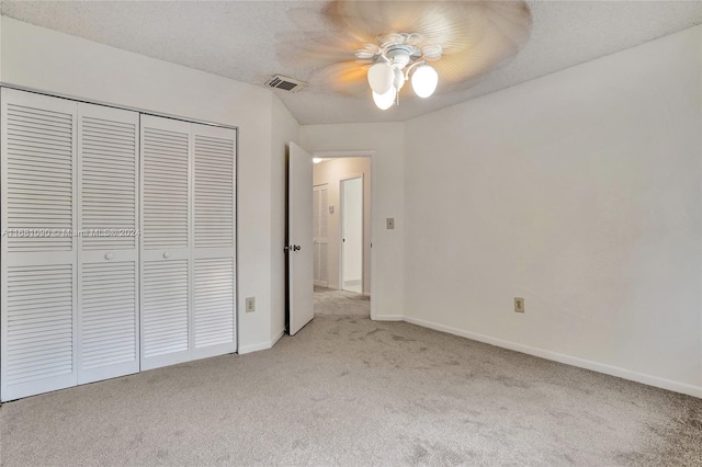 unfurnished bedroom with a textured ceiling, light colored carpet, a closet, and ceiling fan