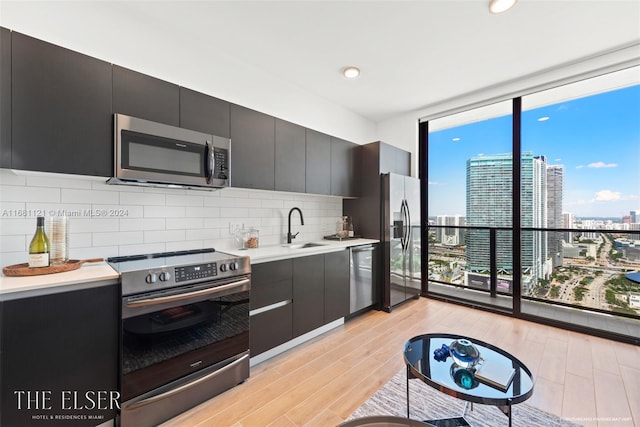 kitchen with tasteful backsplash, appliances with stainless steel finishes, sink, and light wood-type flooring