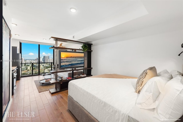 bedroom with expansive windows, wood-type flooring, and access to exterior