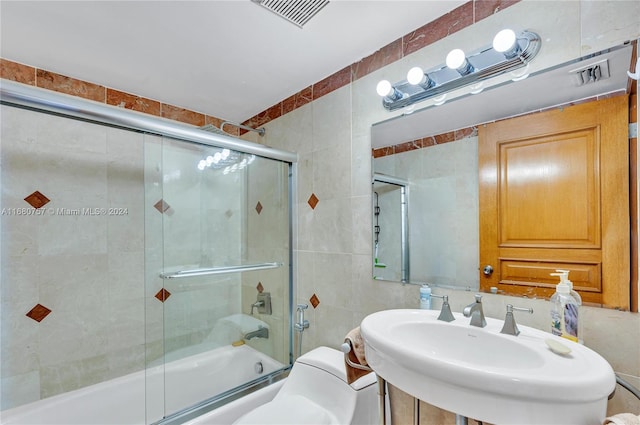 full bathroom with toilet, tile walls, sink, and shower / bath combination with glass door