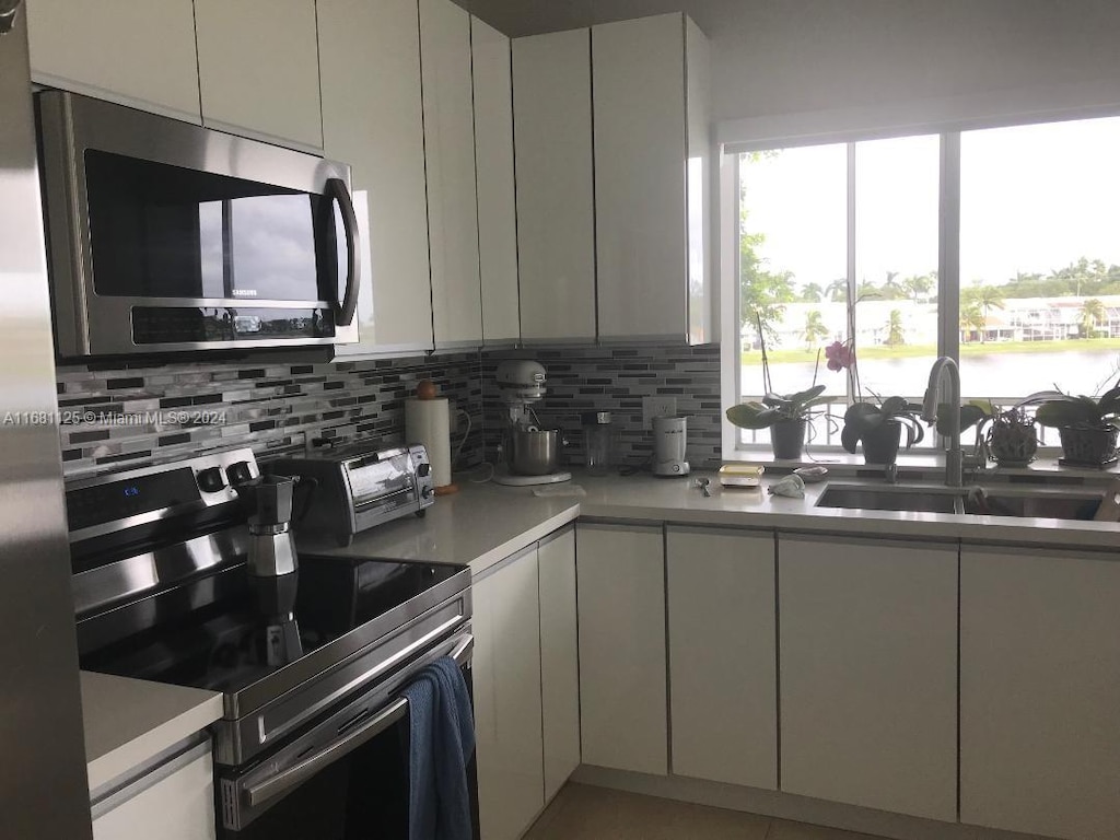 kitchen with tasteful backsplash, appliances with stainless steel finishes, sink, white cabinets, and a water view