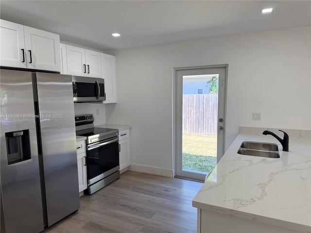 kitchen featuring light stone counters, stainless steel appliances, light wood-style floors, and a sink