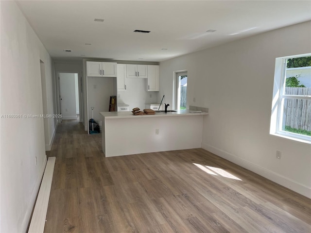 kitchen with kitchen peninsula, hardwood / wood-style floors, white cabinets, and sink