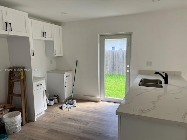 kitchen featuring light stone countertops, light hardwood / wood-style flooring, white cabinetry, and sink