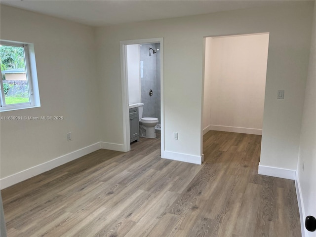unfurnished bedroom featuring light wood finished floors, ensuite bath, a walk in closet, and baseboards