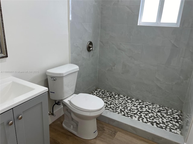 bathroom with tiled shower, hardwood / wood-style flooring, vanity, and toilet