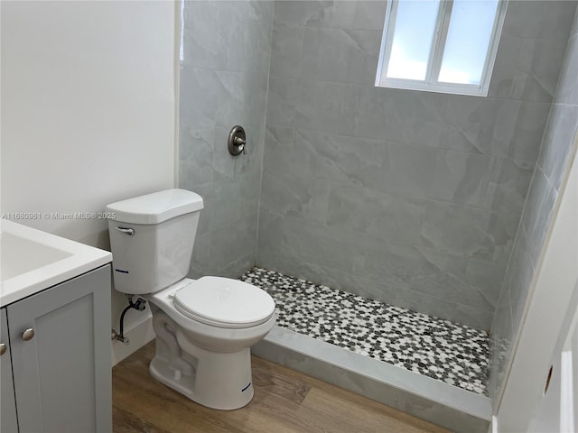 bathroom with tiled shower, hardwood / wood-style floors, vanity, and toilet