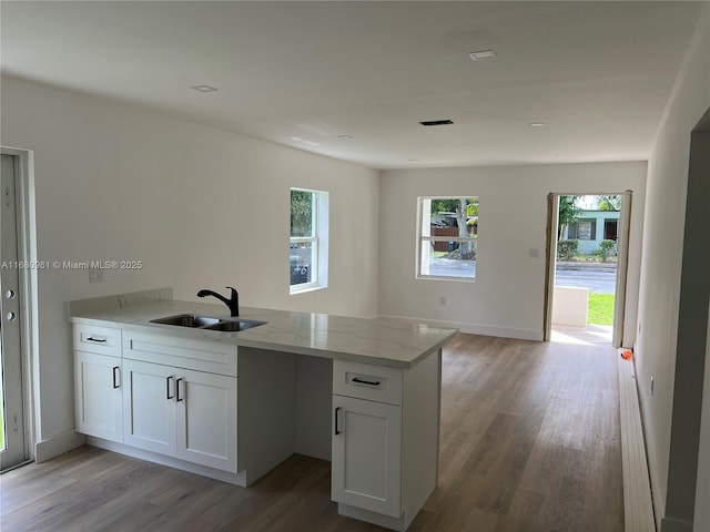 kitchen featuring light stone countertops, kitchen peninsula, light wood-type flooring, sink, and white cabinetry