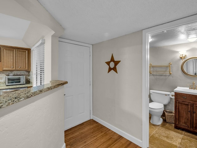 interior space featuring toilet, vanity, wood-type flooring, and a textured ceiling