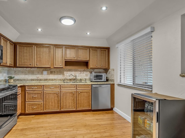 kitchen with light stone countertops, beverage cooler, appliances with stainless steel finishes, light hardwood / wood-style floors, and sink