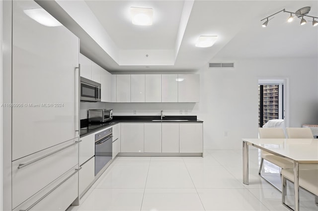 kitchen featuring sink, white cabinets, a raised ceiling, light tile patterned floors, and appliances with stainless steel finishes