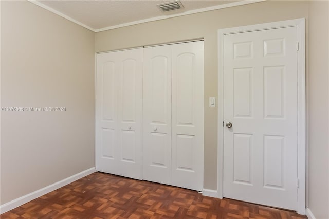 unfurnished bedroom featuring ornamental molding, a closet, dark parquet flooring, and a textured ceiling