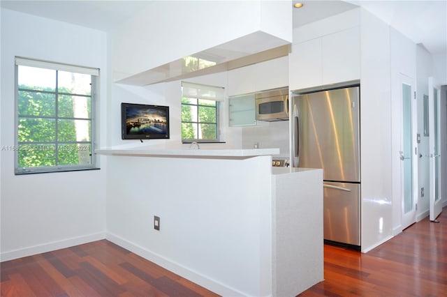 kitchen with kitchen peninsula, appliances with stainless steel finishes, white cabinetry, dark wood-type flooring, and plenty of natural light