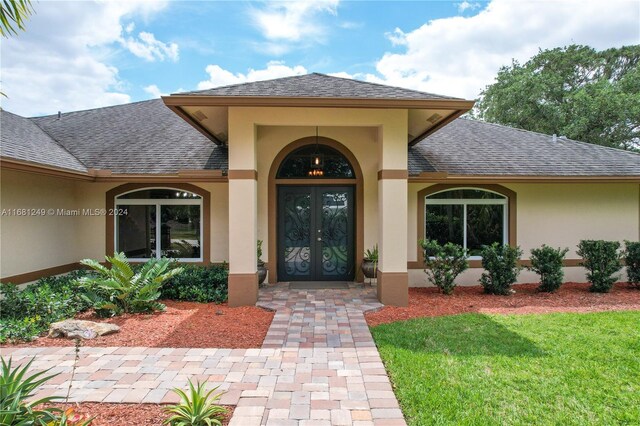 12288 N 82nd Ln N, West Palm Beach, FL 33412 - view of exterior entry with french doors, roof with shingles, stucco siding, and a yard