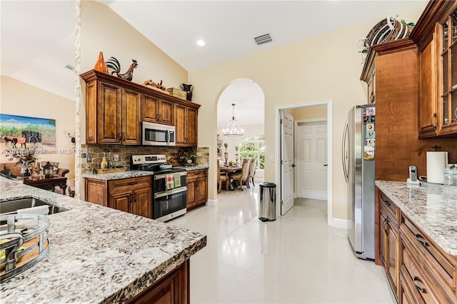 kitchen featuring tasteful backsplash, light stone counters, stainless steel appliances, light tile patterned floors, and an inviting chandelier