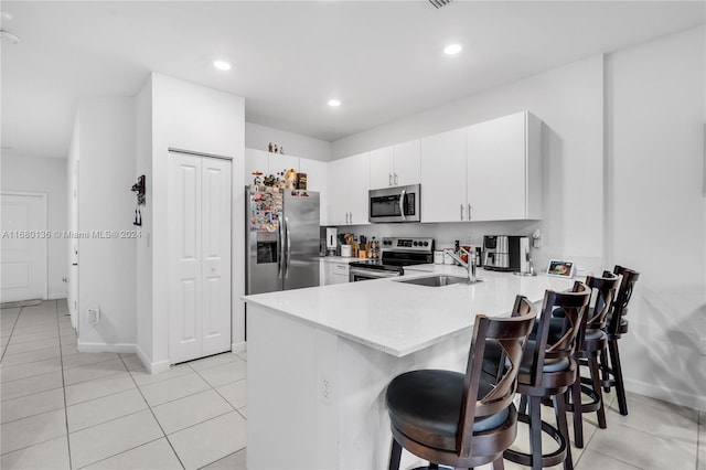 kitchen with kitchen peninsula, a breakfast bar, white cabinetry, sink, and stainless steel appliances