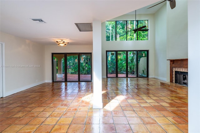 unfurnished living room with a tiled fireplace, a high ceiling, plenty of natural light, and ceiling fan