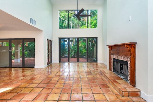 unfurnished living room with a towering ceiling, light tile patterned flooring, a fireplace, and ceiling fan