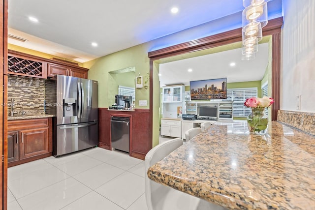 kitchen with appliances with stainless steel finishes, light tile patterned flooring, sink, pendant lighting, and light stone counters