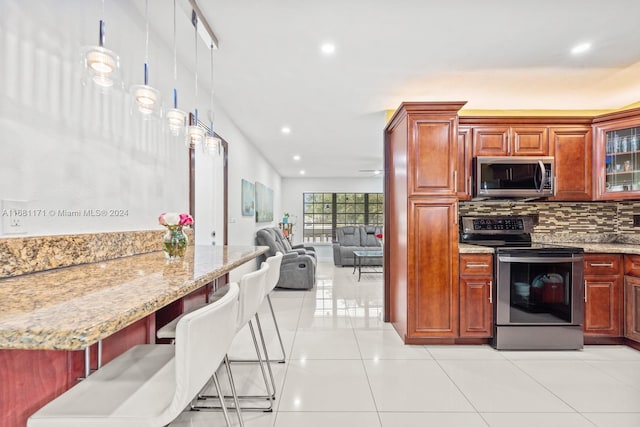 kitchen with light tile patterned floors, appliances with stainless steel finishes, light stone countertops, a kitchen bar, and decorative light fixtures