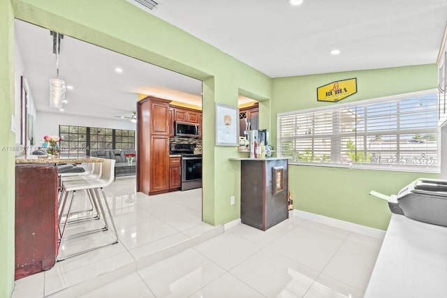 kitchen with vaulted ceiling, a kitchen bar, decorative light fixtures, light tile patterned flooring, and appliances with stainless steel finishes