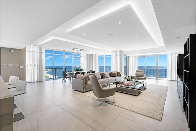 tiled living room with expansive windows, a tray ceiling, and a water view