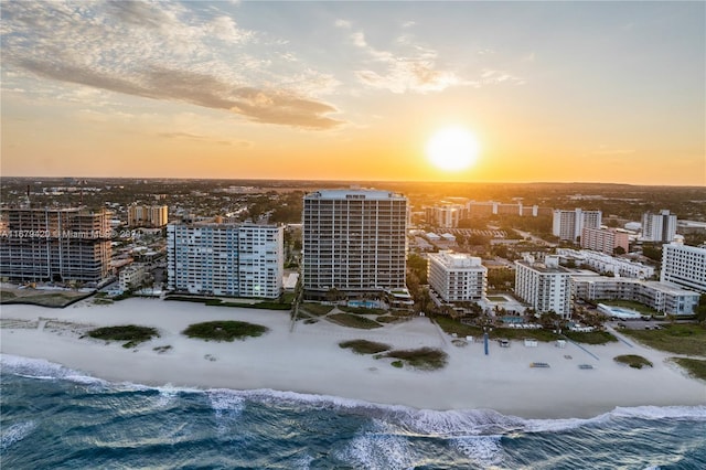 aerial view at dusk featuring a water view and a beach view