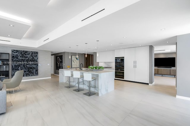 kitchen with white cabinets, hanging light fixtures, a kitchen island with sink, a kitchen bar, and sink