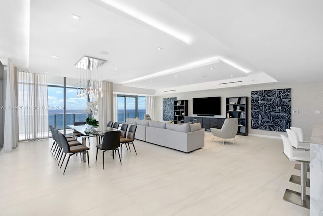 living room with a chandelier, a water view, and a raised ceiling