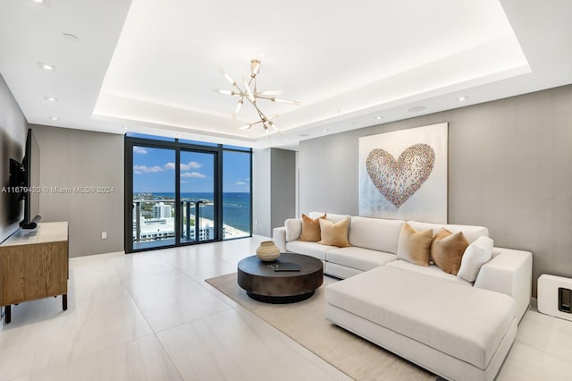 living room with light tile patterned flooring, a tray ceiling, expansive windows, a water view, and an inviting chandelier